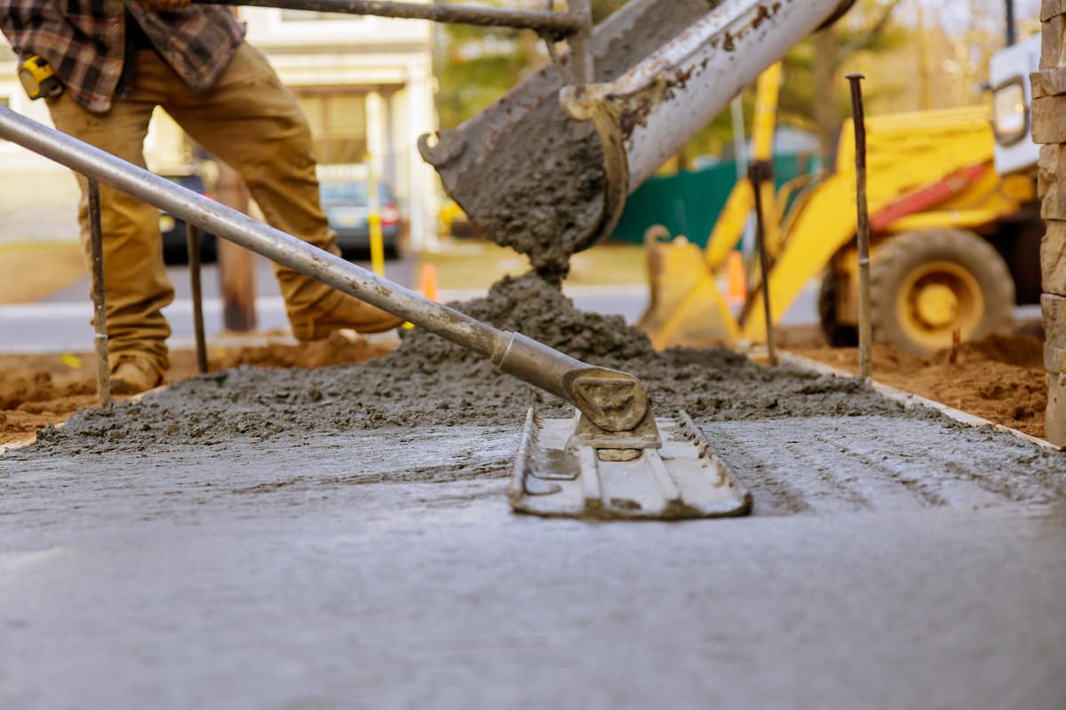Worker pouring and smoothing fresh concrete for a new pavement installation.
